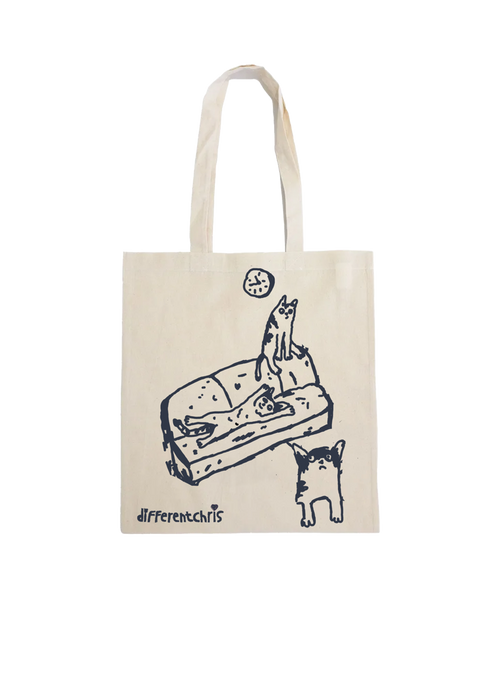 An off white canvas tote bag with a black line art illustration of a cat on a sofa and the text 'differentchris' printed near the bottom.